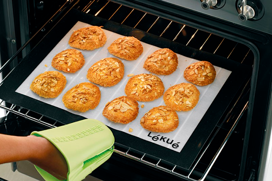 Galletas colocadas sobre un tapete de silicona en una bandeja que está siendo introducida a un horno