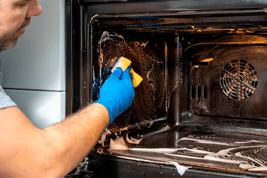 Hombre limpiando un horno aplicando uno de los consejos para mantener tus equipos de cocina