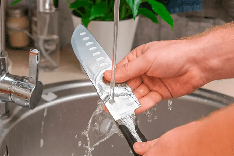 Manos de hombre limpiando un cuchillo aplicando uno de los consejos para mantener tus equipos de cocina