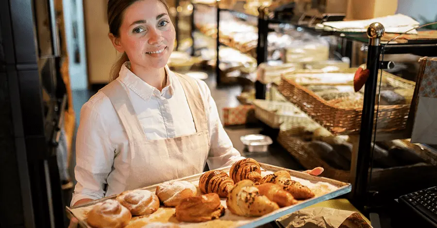 Mujer panadera sosteniendo una charola con varios panes