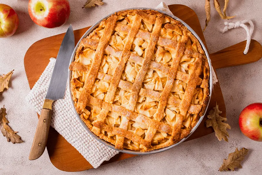 Vista superior de una tarta de manzana con algunas manzanas y un cuchillo alrededor