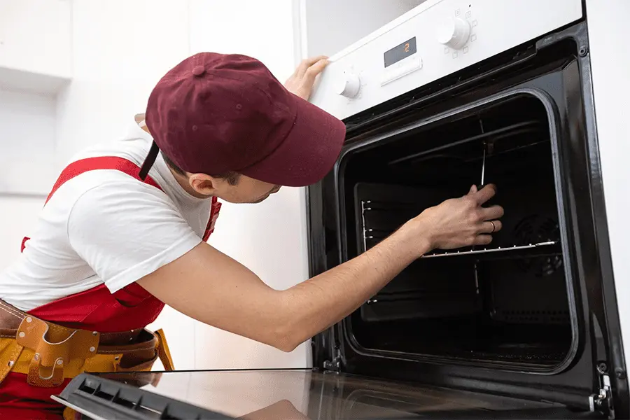 Joven reparador arreglando horno con destornillador