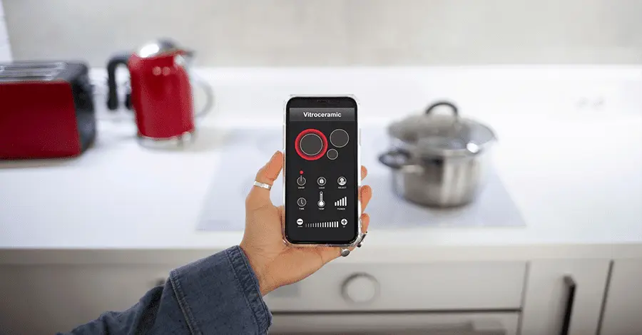 Mano de mujer sosteniendo un teléfono que manipula mediante una app la cocina