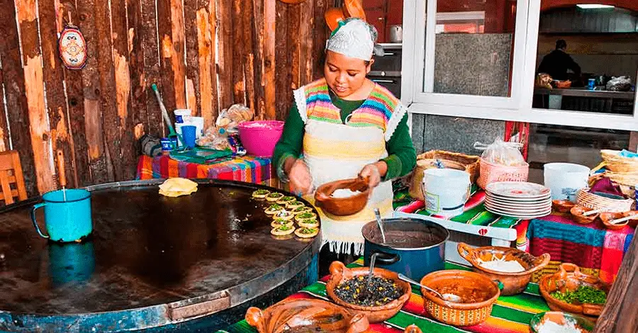 Mujer mexicana en una cocina tradicional utilizando equipos para preparar antojitos mexicanos para las fiestas patrias
