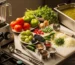 Marmita y licuadora industrial en cocina profesional; mesa con jitomates, tomatillos, chiles guajillo, serrano y pasilla, cebolla y cilantro; gran recipiente con salsa verde y roja, luz cálida que resalta frescura y volumen de producción.